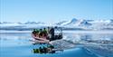 An open RIBboat travels through Arctic waters surrounded by snow-covered mountains.