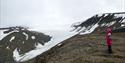 Two small people pointing at a snow covered valley with a mountin in the background