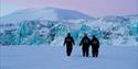 Tre personer går foran en blå isbre.
