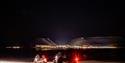 Two snowmobiles in the foreground with town lights from Longyearbyen in the background surrounded by the darkness of night