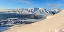 A person skiing down a mountain with Longyearbyen and a mountainous landscape in the background