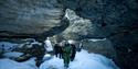 A group walking through a narrow rock passage in winter terrain.