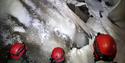 Three people with headlamps and helmets admiring the formations on the ceiling of the ice cave.