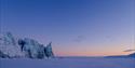 Pastel colours and blue light in the sky above a glacier front and a flat snow-covered plain of sea ice