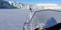 Snowmobiles driving in a line with a glacier in the background