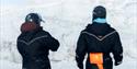 Two persons wearing snowmobileclothings, seen from behind.