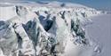 Sharp ice formations and blue ice covered with snow at a glacier front.