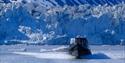 A boat in the foreground sailing away from a glacier in the background