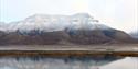 Hiorthfjellet om høsten, med nysnø på toppen. Fjellet speiler seg i Adventfjorden.