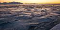 Frozen sea with cracks and drifting ice under a golden sunset.