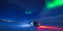 Northern lights over snow covered mountains with a snowmobile in the front