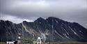 Bygningene på Isfjord Radio Adventure Hotel sett utenfra med et fjell og en overskyet himmel i bakgrunnen