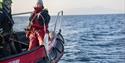 A guide next to a guest in a RIB boat where the guest is holding a fishing pole with a hooked fish hanging in the air next to the boat