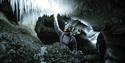 A guide with a bright head lamp and helmet inside an ice cave feeling one of the icicles hanging from the cave roof