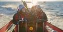 A group of guests on board a RIB boat sailing at speed in a fjord with sunshine on the fjord in the background