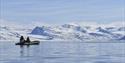 Four persons in a rubber boat on a calm fjord with snow-covered mountains in the background