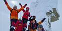 A group of guests cheering for the camera on top of Trollsteinen in snowy conditions