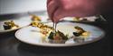 A chef preparing a dish on a plate with pincers