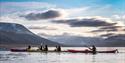 People kayaking in a fjord in the foreground, with a valley and mountains in the background.
