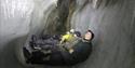 Four people lie on the ground in the ice cave, illuminating the icicles hanging down from the ceiling.
