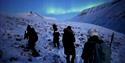 Several persons hiking in the snowcovered mountains. northern lights in the background