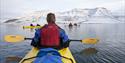 Personer padler kajakk i adventfjorden. Hiortfjellet ses i bakgrunnen