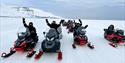 Several persons on a snowmobiletour, having a break and waving to the camera