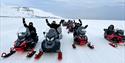 Flere personer på snøscootertur, har pause og vinker til kameraet