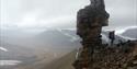 A person and a dog on a mountain trip standing next to a pillar of rocks