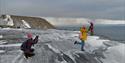 Three people posing to take a photo on snowcovered grounds with a mountain and the ocean in the background