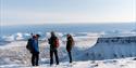 several people standing on top of snowcovered mountain. overlooking plateaus and other mountains in the background