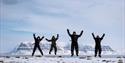 Fire personer hopper og jubler på snødekt tundra i Arktis.