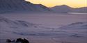 Snødekte daler og fjell under en gyllen solnedgang, med snøskutere parkert i forgrunnen.