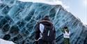 Two peoplel looking up at a massive blue ice wall.