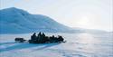 Flere snøscootere står parkert i et snødekt landskap. sola og fjell ses i bakgrunnen