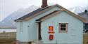 A blue building in Ny-Ålesund known as the post office, seen from the outside with mountains in the background