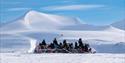 Snøscootergruppe i arktisk vinterlandskap.