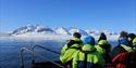 Several people in a small open RIB boat, enjoying the view of the mountains in the background