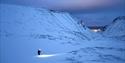 Person hiking in the mountains during dark season and blue hour. Light from the headlamp lights up the snow.
