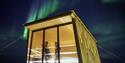 Two persons in the sauna at Isfjord Radio looking out through a window. Outside it's dark with stars and northern lights in the skies.