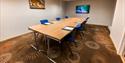 A small conference room with tables, chairs and a screen in the end of the room