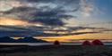 Three tents on the ground with mountains and sunset in the background.