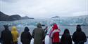 A group of guests on board a boat looking towards a glacier front by a fjord in the background