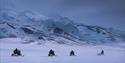 A guide and guests on snowmobiles in a landscape with mountains in the background