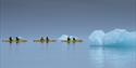 Three kayaks with guests paddling between nearby floating icebergs