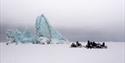 Guests and a guide on snowmobiles taking a break by an iceberg frozen in sea ice