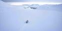 A snowcat on a glacier driving along tracks in the snow towards Longyearbyen in the background