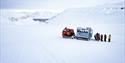 Guests and a guide standing next to a snowcat on top of a glacier surrounded by snow-covered mountains