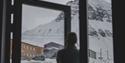 A guest in silhouette in the foreground looking up at a mountain and colourful buildings in snowy surroundings in the background