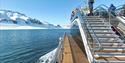 A boat sailing through a fjord with guests on board and snow-covered mountains in the background